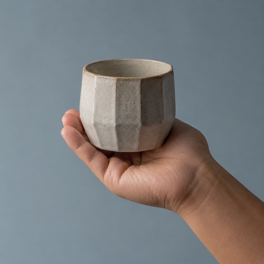 A hand holding the Faceted Handleless 220 ml, showing the scale of the cup against a hand