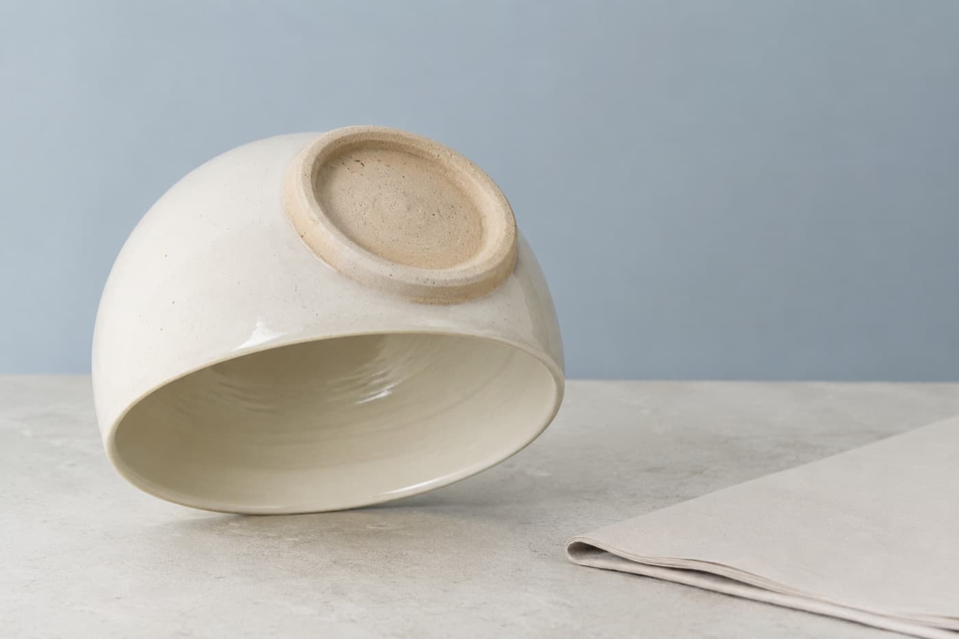 A stoneware cup turned upside down showing its unglazed foot ring and glazed interior, beside a folded paper document